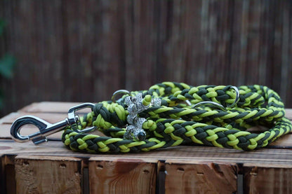 Geflochtene Hundeleine aus Paracord in Limettengrün und Olivgrün mit Metallkarabiner und zwei silbernen anhängern auf Holztisch