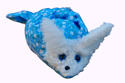 Kuscheltier in Form eines weißen Hasenkopfes mit Knopfaugen, eingewickelt in blauem Blümchen Stoff 