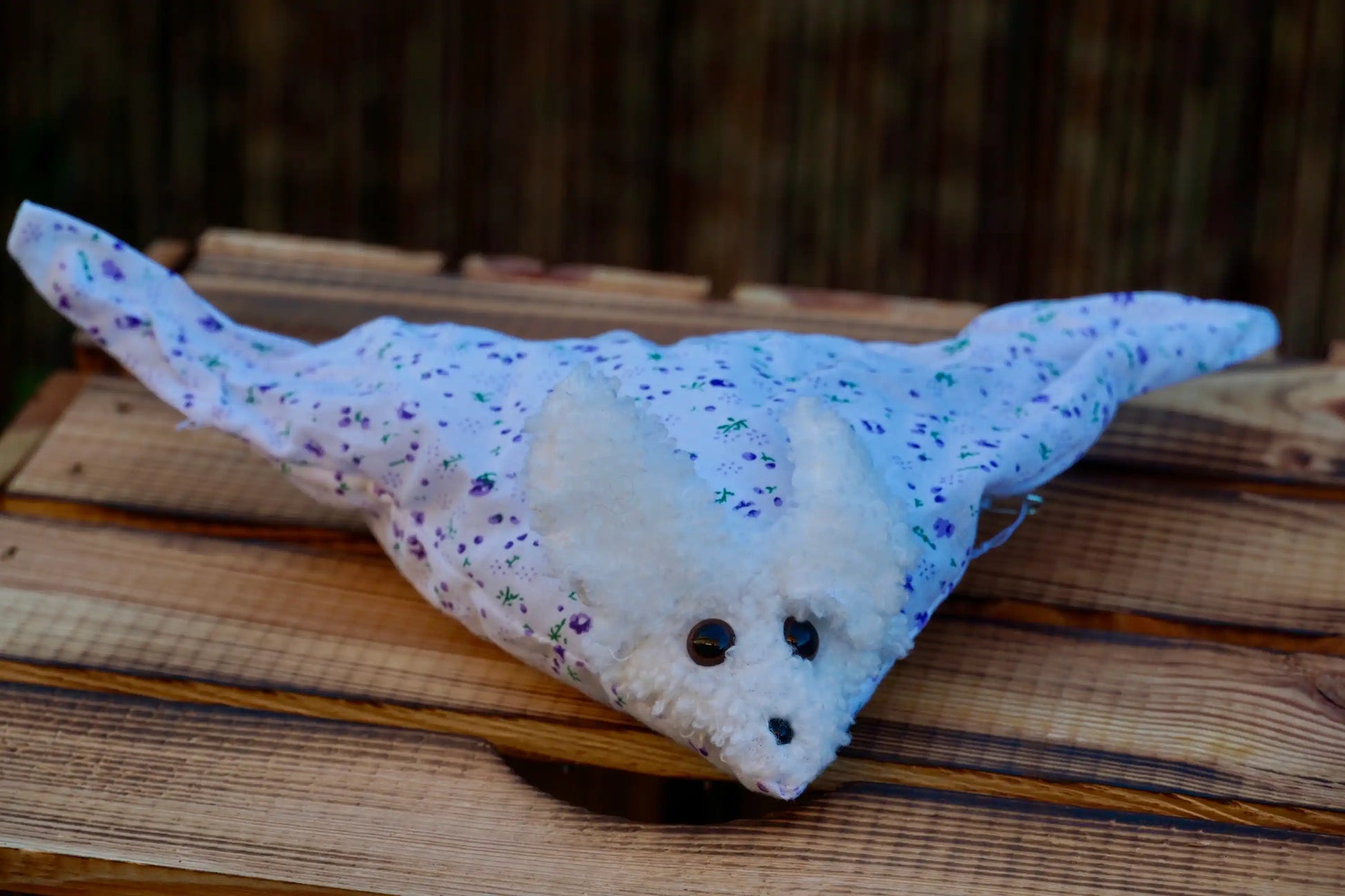 Kuscheltier in Form eines weißen Hasenkopfes mit Knopfaugen, eingewickelt weißem Blümchen Stoff auf Holztisch