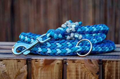Geflochtene Paracord Hundeleine in Blautönen mit Metallkarabiner und Schmuckperlen am Griff auf Holzkiste
