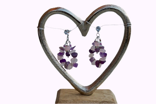 Herzförmiger Schmuckhalter aus Metall mit zwei Ohrringen aus Amethyst und Rosenquarz Steinen, auf Holzsockel.