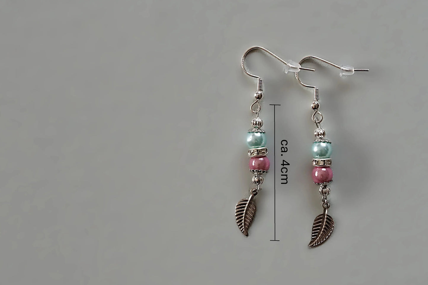 Ohrringe mit silberfarbenen Haken, zwei Perlen in Türkis und Rosa sowie einem silberfarbenen Blattanhänger mit Maßstab