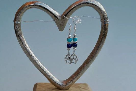 Ohrringe mit silberfarbenen Haken, zwei Edelsteinperlen in Turquenit und Sodalith sowie einem silberfarbenen Hundepfotenanhänger aufgehängt an einem herzförmigen Metallständer.