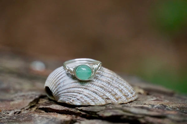 Ring mit einer grünen Aventurin Edelsteinperle eingefasst in versilbertem Kupferdraht, platziert auf einer Muschel