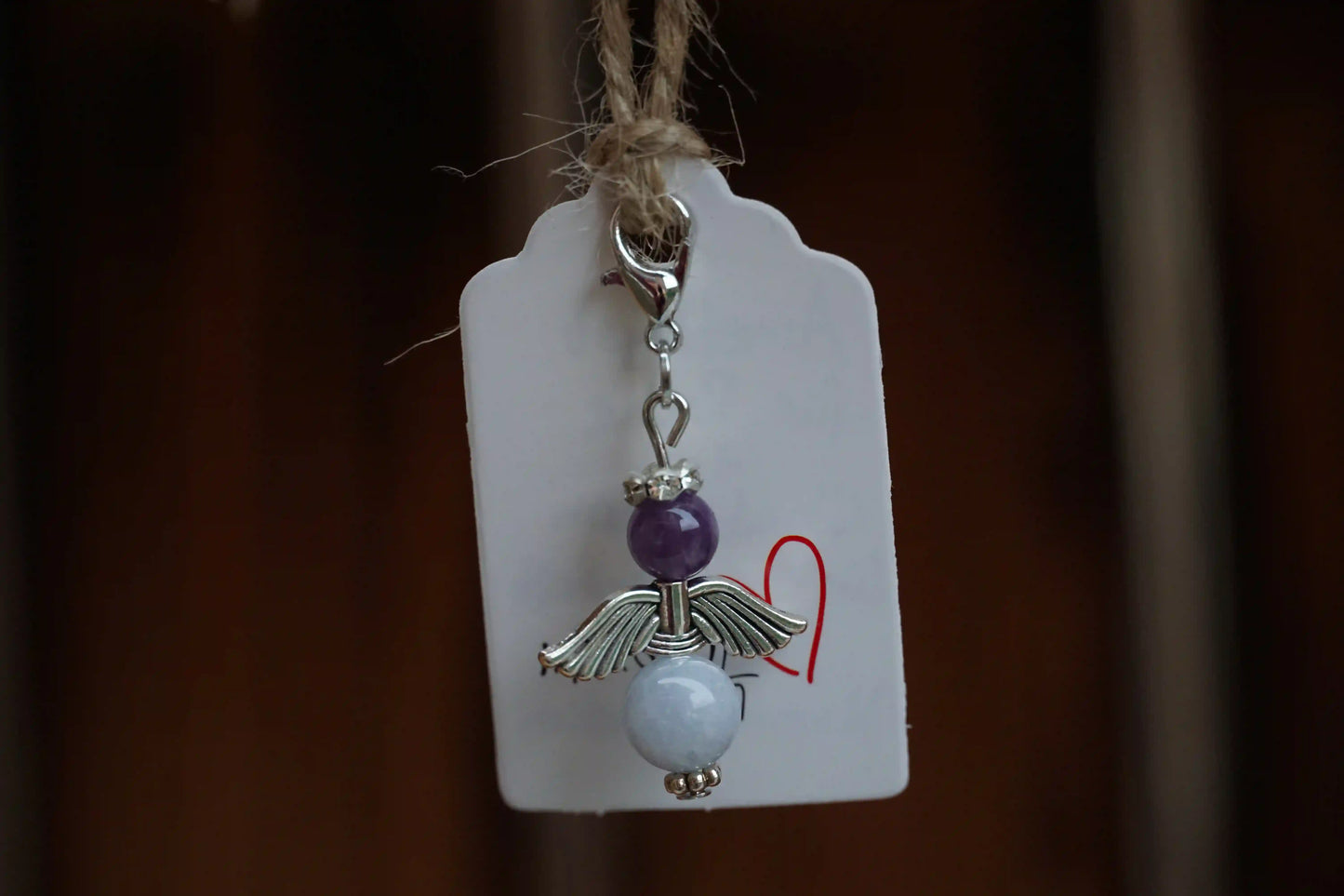 Anhänger in Form eines Schutzengels mit Amethyst- und Chalcedonperlen, silberfarbene Flügel, an einem Band befestigt.