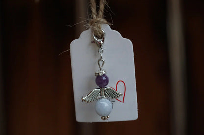 Anhänger in Form eines Schutzengels mit Amethyst- und Chalcedonperlen, silberfarbene Flügel, an einem Band befestigt.