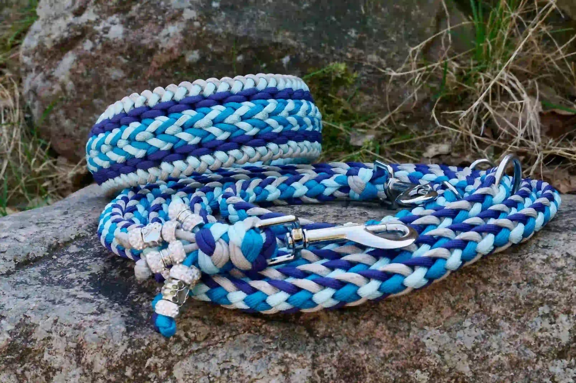 Geflochtene Hundeleine und Halsband in Blau- und Grautönen mit Metallkarabinern und Zierperlen auf einem Stein