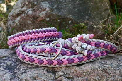 Geflochtene Hundeleine und Halsband in Lila- und Grautönen mit Metallkarabinern und Zierperlen auf einem Stein