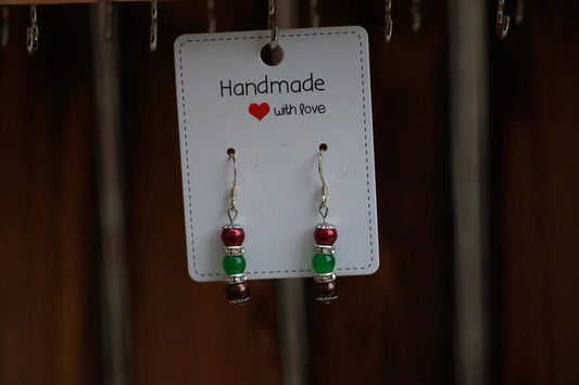 Ohrringe mit roten, grünen und brauen Perlen, an einer Karte mit der Aufschrift 'Handmade with love'.