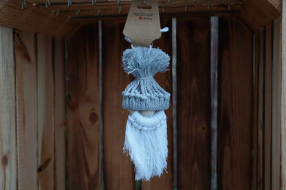 graue gestrickte Mütze mit Bommel auf einer Holzfigur mit weißem, langem Bart, hängend vor Holzlatten.