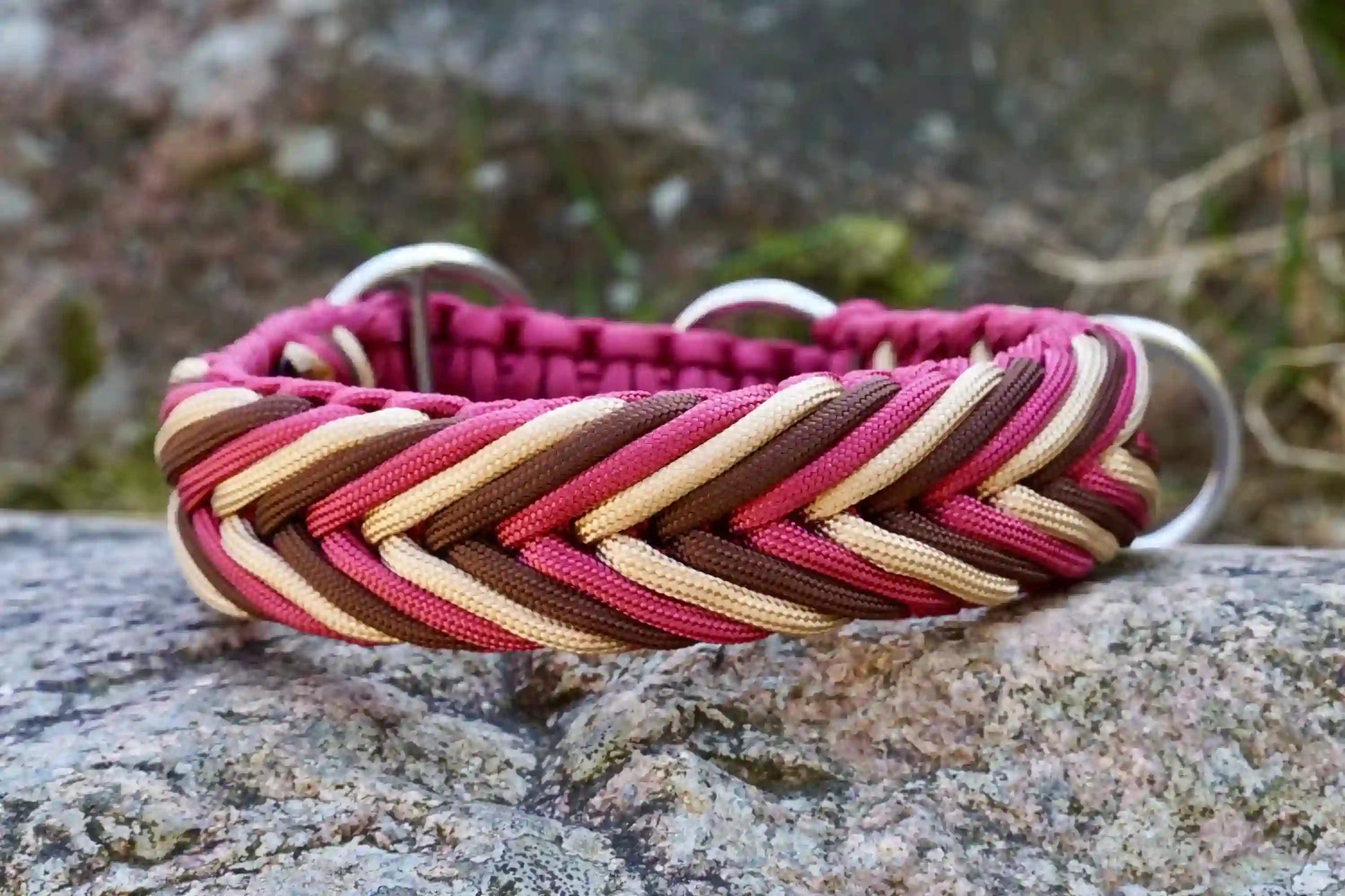 Geflochtenes Hundehalsband in Rot-, Beige- und Brauntönen mit Metallringen auf einem Stein