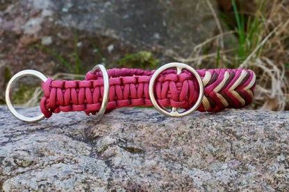 Geflochtenes Hundehalsband in Rot-, Beige- und Brauntönen mit Metallringen auf einem Stein