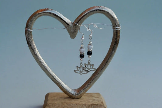 Ohrringe mit silberfarbenen Haken, zwei Edelsteinperlen in Magnesit und Turmalin sowie einem silberfarbenen Lotusblumenanhänger aufgehängt an einem herzförmigen Metallständer.