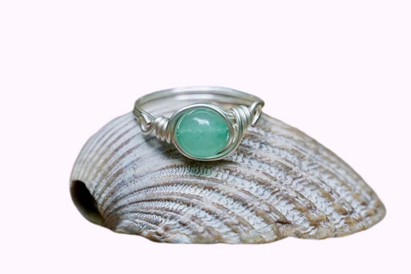 Ring mit einer grünen Aventurin Edelsteinperle eingefasst in versilbertem Kupferdraht, platziert auf einer Muschel